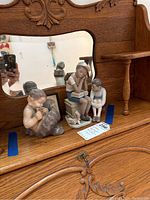 Two porcelain figures on an antique wood dresser with mirror - one of Pan playing flute and one of boy reading to girl