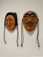 Two traditional carved wooden masks hanging on a wall, showing full front view of both masks.