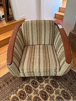 Frontal view of chair showing barrel back shape, striped fabric and wood armrests