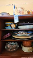 Shelf with mixed plates, bowls including blue and white pottery, metal bowl and Pyrex measuring jug.