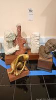 Five sculptures on wooden bases arranged against a wall, including busts and abstract figures.
