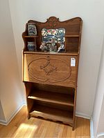 Full front view of the wooden secretary desk with fold-down writing surface, mirror, and shelves holding decorative items.