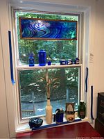 Window display showing stained glass panel and assorted blue glass items on windowsill