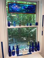 View of window with framed stained glass panel and various blue bottles on windowsill