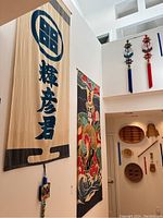 Two tall vertical fabric tapestries with Asian characters and colorful warrior design on wall.