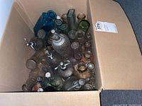Top view of an open box filled with various vintage glass bottles in multiple colors including clear, blue, green, and amber.