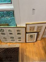 Four framed wall art pieces leaning against a wall, showing two gold-colored frames and two smaller framed prints.
