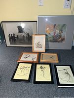 Full lot of eight wall art pieces arranged on carpet showing variety of styles and frames.