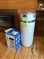 Full view of the Homedics air purifier next to the replacement filter box and power cord on wooden floor.