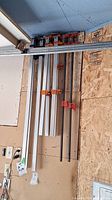Overview showing five pipe bar clamps hanging on a wall, with varying sizes from 36 to 48 inches, featuring both aluminum and metal pipes with red and blue clamp heads.