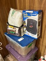 Photo of the lot items stacked showing the Dr. Scholl's back cushion box, king size sheets in white packaging, and the sofa cover in black zippered case