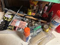 Photo showing hydraulic bottle jacks, multiple spray cans, grease gun and applicator, tire gauges, multipurpose ties, ratchet tie downs with 14' straps, ice scrapers, and trailer hitch accessory all arranged on a shelf.