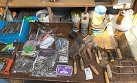 Wide view of the workbench showing multiple hand tools, trowels, containers, and various items spread out