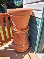 Stack of three rolled rim clay pots and two clay saucers stacked underneath against house siding outdoors in daylight.