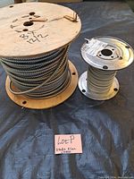 Two rolls of electrical cable on a table with handwritten note identifying them as 2 rolls electrical cable. Larger wooden spool roll is BX cable 14/2, smaller metal spool roll is white nylon 14/2 cable.