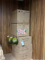 Stacked cardboard boxes labeled with counts of small and large coconuts; three loose green coconuts hanging on side