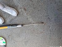 Pressure washer wand extended showing metal nozzle and yellow fiberglass body near feet for scale