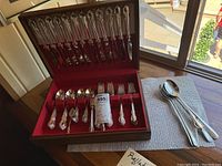 Complete silverplated flatware set arranged in original case with red interior lining, showing knives, forks, and spoons with ornate handles.