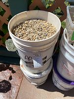 Two stacked white plastic pails outdoors, top one open filled with Jasper stones