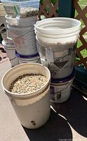 Three white plastic pails stacked and placed outdoors, filled with small, smooth, multi-colored Jasper stones.