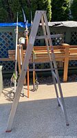 Full view of the 6ft aluminum ladder set in A-frame position outdoors with background of patio furniture and garden tools.
