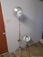 Two aluminum photography light stands side by side with reflector lamps, one fully extended and one folded.