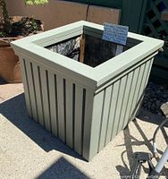 Full outside view of the green stained cedar square planter showing vertical slats and overall shape.