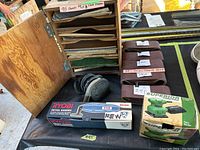 Photo showing Ryobi detail sander in box, Porter-Cable orbital sander, plywood sandpaper rack with many sandpaper sheets inside.