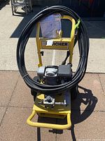 Front view of Karcher pressure washer with long black hose coiled on the yellow frame and the motor visible.