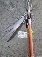 Close-up photo of the pruning saw blades bundled together with the extendable pole handle shows the label describing the item.