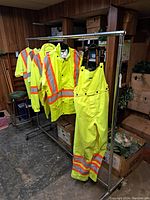 High visibility yellow Viking Professional Journeyman 300D rain overalls and jackets hung on a garment rack in a basement with visible wood panel walls and storage boxes.