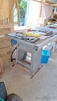 Front view of table saw on metal stand with assorted accessories on top