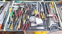 Wide shot of diverse hand tools laid out on a black surface including various screwdrivers, pliers, hammers, wrenches, clamps, saws and chisels.