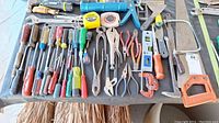Top view of assorted hand tools including screwdrivers, pliers, measuring tapes, wrenches, hammers, levels, and saws spread on dark cloth
