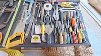 Overview of hand tools on black cloth including saws, pliers, hammers, screwdrivers, and tape measure