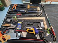 Full view of assorted hand tools spread on surface including hammers, pry bars, hand saws, caulking gun, and measuring tools.