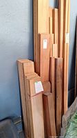 Front view of bundled wood boards leaning against wall, mixed lengths