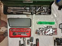 Photo showing green S-K Tools metal case with metric sockets and ratchets, loose sockets and attachments, small gray case with imperial sockets and ratchet inside, plastic bag with imperial sockets.