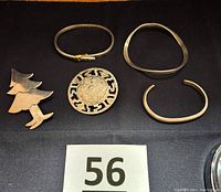 Five Mexican silver jewelry pieces arranged on black cloth: two brooches and three bangle bracelets