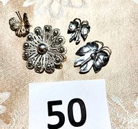 Top view of four silver pins set on fabric background with a number 50 card, showing intricate filigree and decorative etching details.