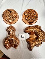Photo showing all four copper molds arranged on a white surface: lobster, curved fish, moon with stars, and four-leaf clover shapes visible with clear detail and shiny finish.