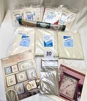 Photo showing various pieces of new counted cross stitch fabric in original packaging, including several sizes of 18-count and 14-count fabric, plus two pattern booklets.