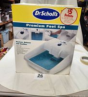 Front of the box shows the Dr. Scholl's Premium Foot Spa with water inside and details like $5 rebate offer, highlighting features like reviving, relaxing, and soothing effects.