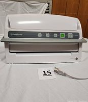 Front view of the white FoodSaver vacuum sealing system showing the closed lid, control buttons, and power cord on a white backdrop.