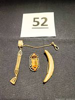 Overview photo of three antique gold-toned jewelry pieces: long mesh chain fob with swivel hook, colorful oblong pin, and crescent brooch.