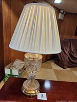 Full view of vintage cut glass lamp with shade on table against wood-paneled wall.