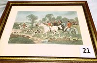 Framed color print showing a Victorian fox hunting scene with riders and dogs in a countryside setting, housed in a gold-tone frame.