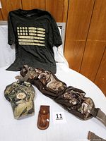 Overview of hunting attire lot showing Bass Pro Shop shirt, camouflage cap, leather cutter holder, and Field & Stream waist pack