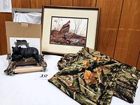 Full view of lot items on a table showing camouflage sheets, framed grouse print, and boxed grizzly bear toilet paper holder.