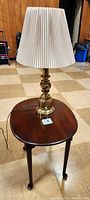 View of the mahogany oval end table with the brass lamp placed on top, showing overall shape and finish of both items.
